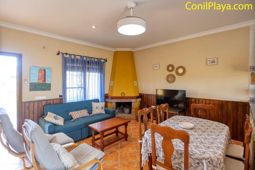 Salón acogedor con chimenea, sofá azul, mesa y comedor en vivienda de alquiler en Conil