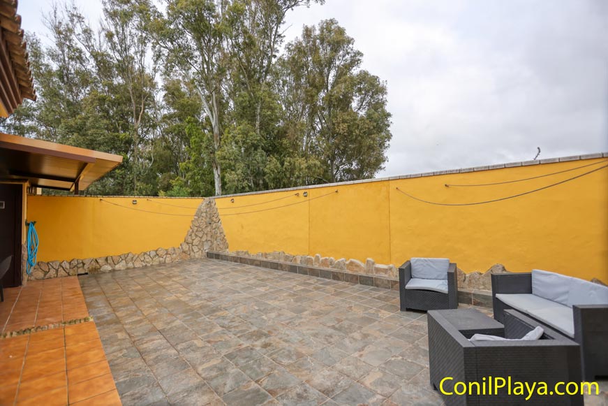 Terraza amplia con muro amarillo, suelo de baldosas y mobiliario exterior sencillo