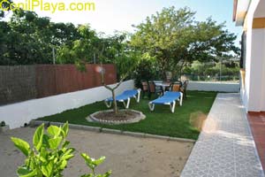 Jardín con césped, tumbonas azules y mesa con sillas junto a un árbol