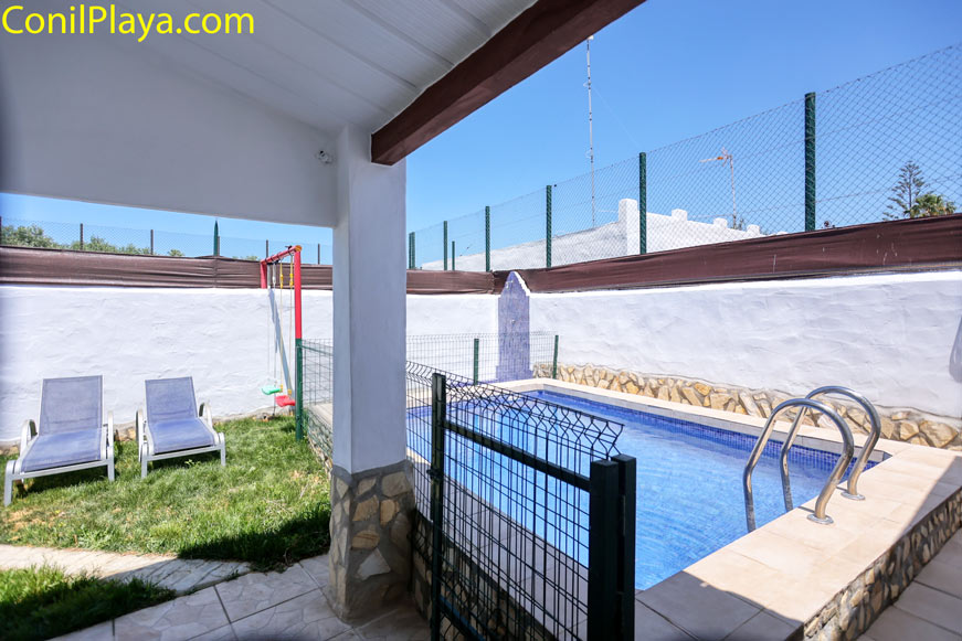 Vista de la piscina desde el porche con mobiliario y césped
