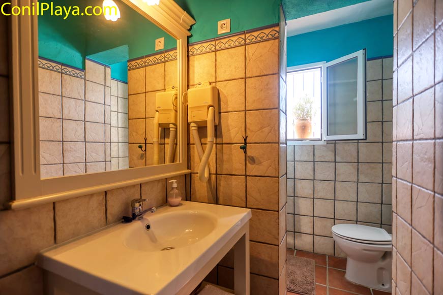 Cuarto de baño con lavabo, espejo, secador y ventana abierta al exterior