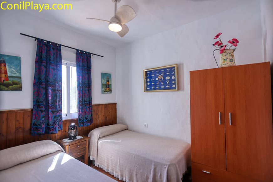 Dormitorio con dos camas individuales, armario, ventana y ventilador de techo