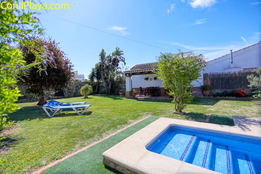 Jardín con césped, piscina pequeña y zona de sombra con mesa y sillas