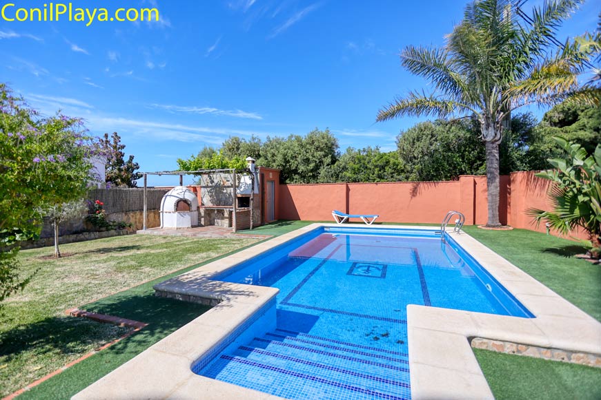 Piscina con escalones en jardín vallado con zona de barbacoa y palmera