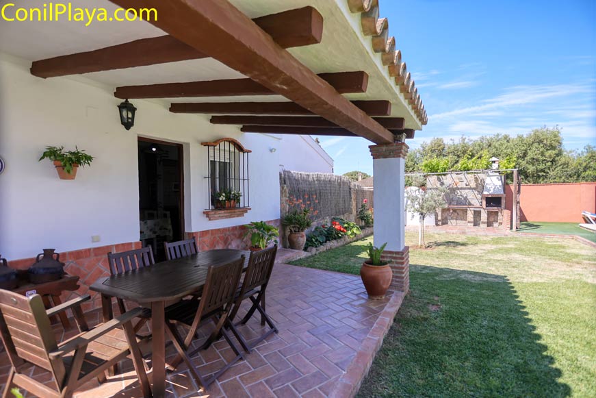 Porche cubierto con mesa y sillas junto a jardín y zona de barbacoa