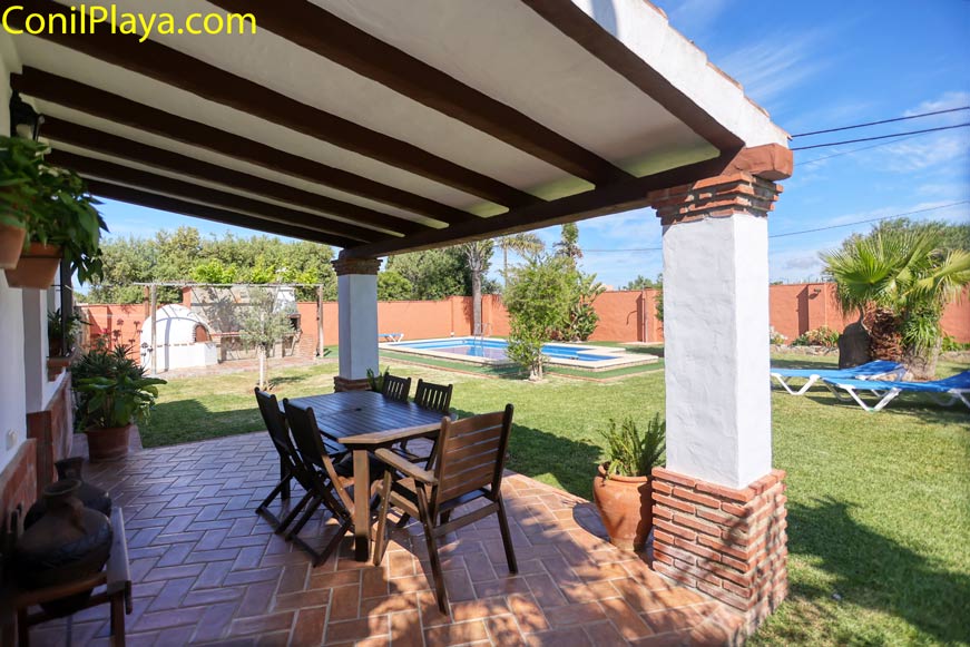 Vista desde el porche cubierto con mesa hacia el jardín y la piscina