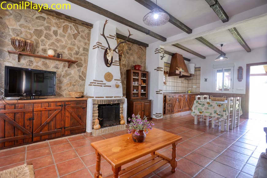 Salón rústico con chimenea, cocina abierta y mesa comedor visible