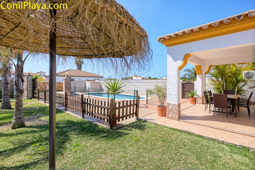 Jardín y piscina exterior Jardín con césped, piscina vallada y porche con mesa y sillas