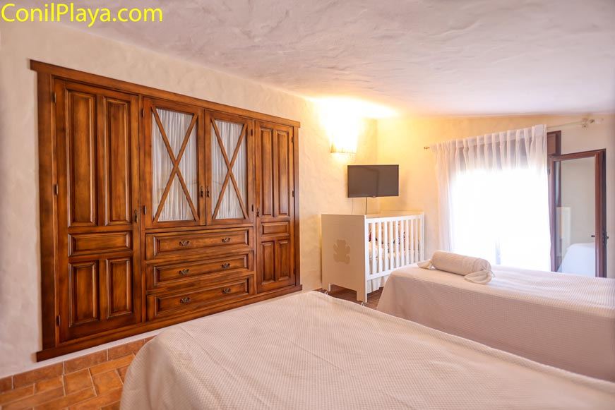 Dormitorio con armario de madera, dos camas individuales y cuna cerca de la ventana