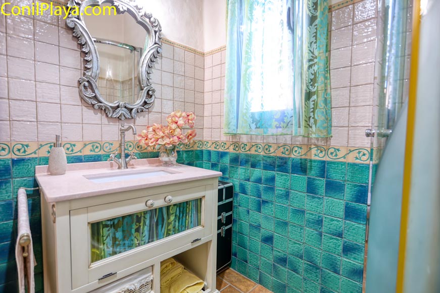 Cuarto de baño con lavabo, espejo decorativo y ventana con cortina verde