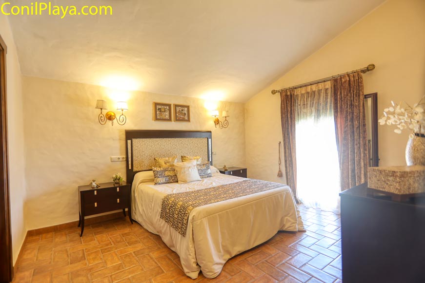 Dormitorio principal amplio con cama doble, mesillas y luz cálida desde la entrada