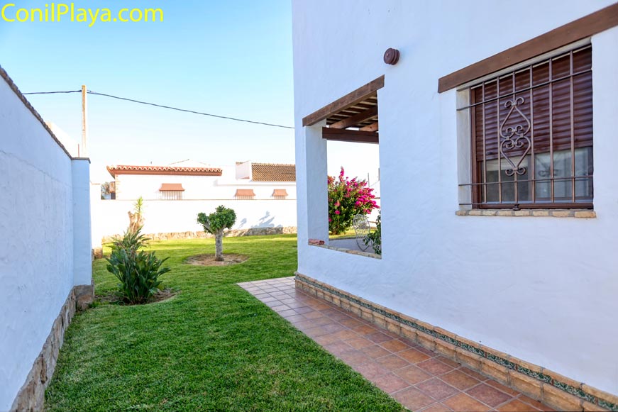 Jardín lateral con césped junto a una casa de pared blanca