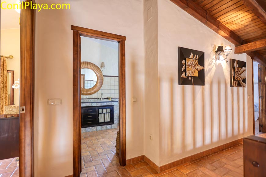 Vista de pasillo rústico con acceso a baño decorado y espejo redondo