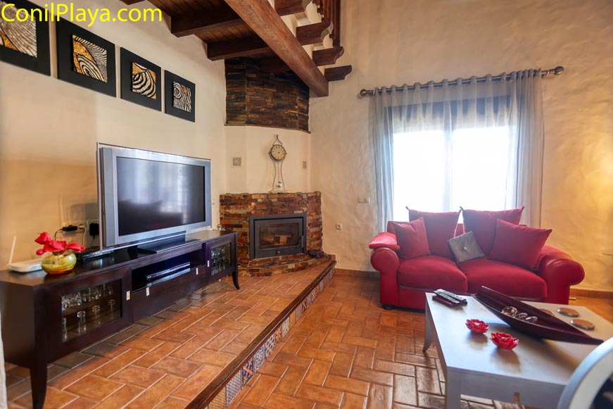 Salón con chimenea televisión sofá rojo y mesa junto a ventana