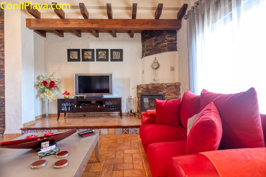 Salón acogedor con sofá rojo, televisión y chimenea vista desde mesa central