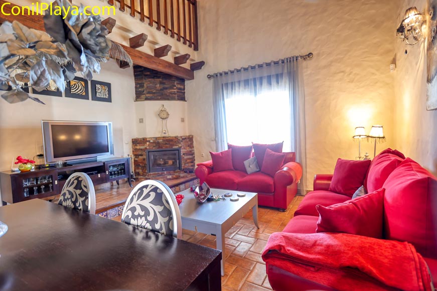 Salón rústico con sofás rojos chimenea y mesa junto a ventana luminosa