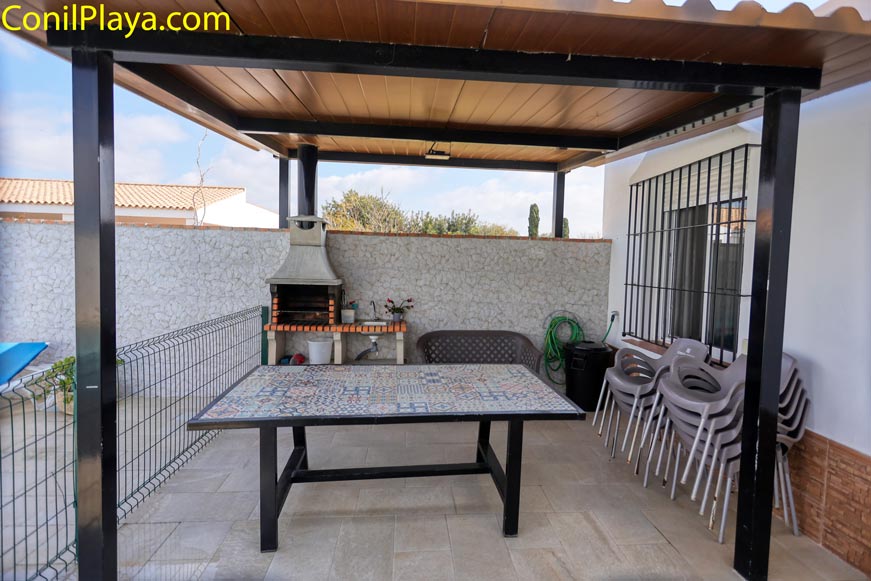 Comedor exterior cubierto con mesa de mosaico y barbacoa al fondo