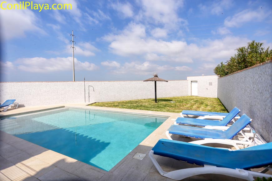 Piscina privada con zona de tumbonas azules y jardín de césped