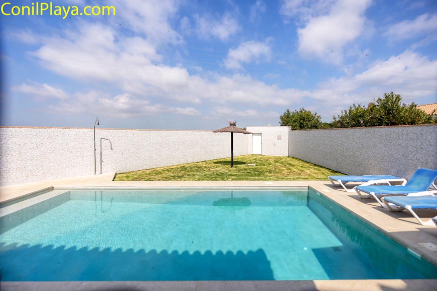 Amplia piscina con sombrilla de paja y jardín vallado