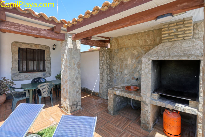 Porche con barbacoa de obra techada junto a mesa y sillas de exterior