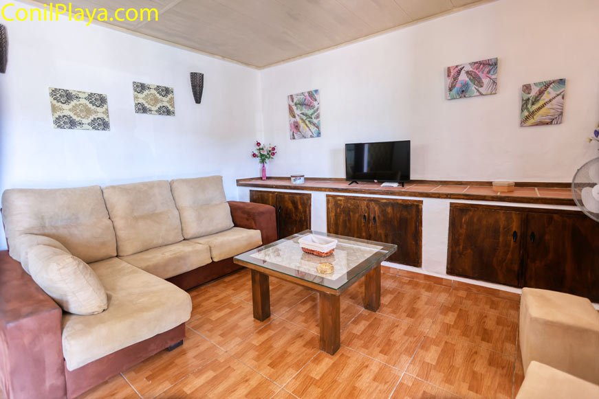Salón con sofá rinconera, mesa de cristal y televisión sobre mueble de madera