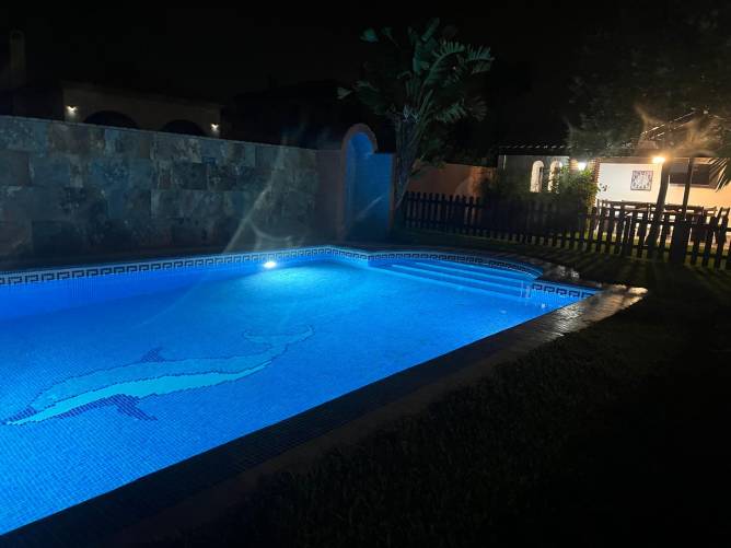 Piscina iluminada junto a jardín y zona de terraza de una casa por la noche