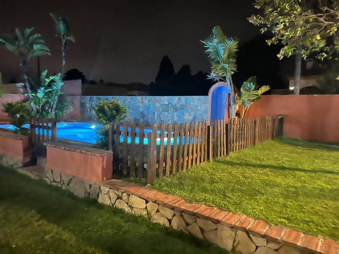 Piscina iluminada por la noche rodeada de césped y valla de madera