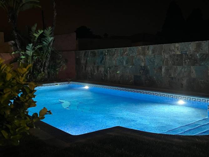 Piscina iluminada por la noche vista desde una esquina del jardín