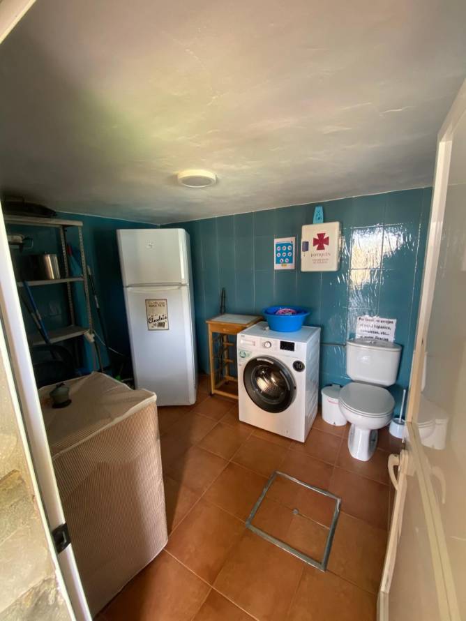 Cuarto de baño con lavadora, nevera y baldosas azules desde la entrada