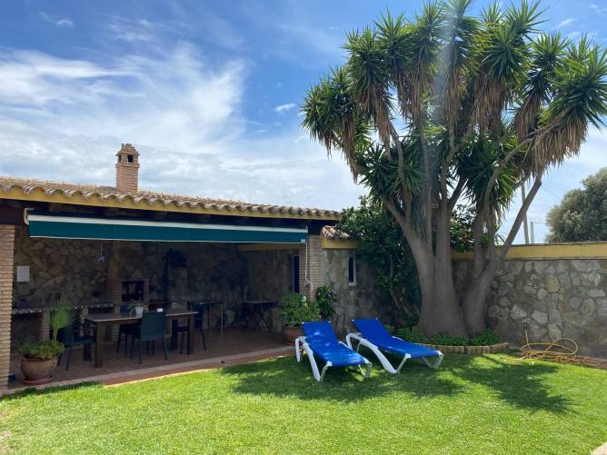 Zona de jardín con barbacoa, tumbonas y césped junto a un porche de piedra