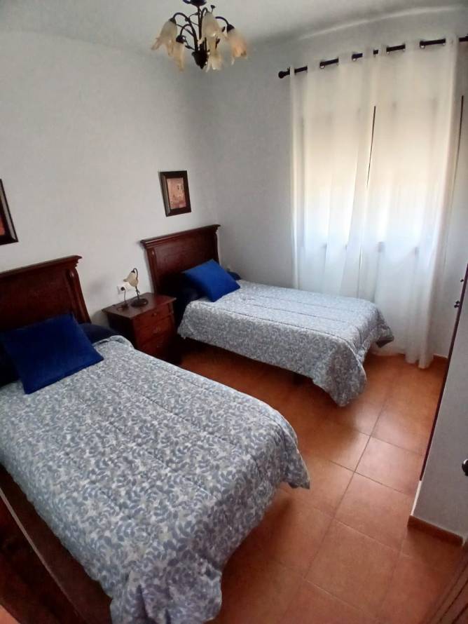 Dormitorio con dos camas individuales y ventana con cortinas blancas
