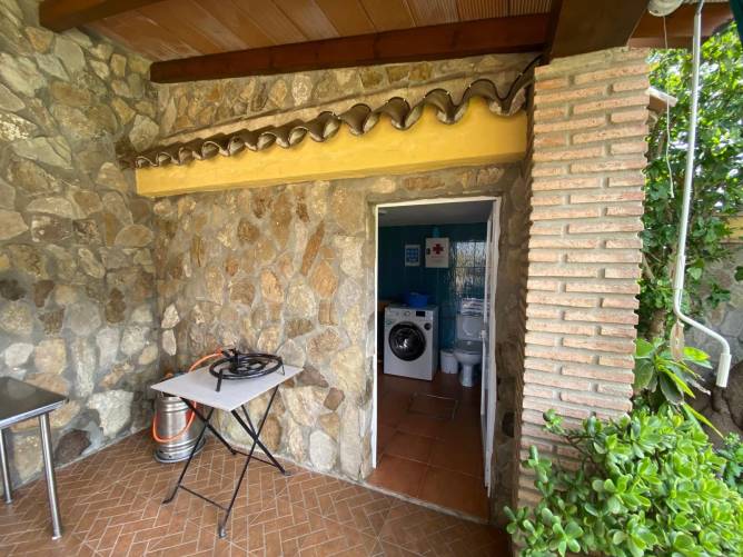 Zona exterior con mesa, paellero y acceso a aseo y lavadora