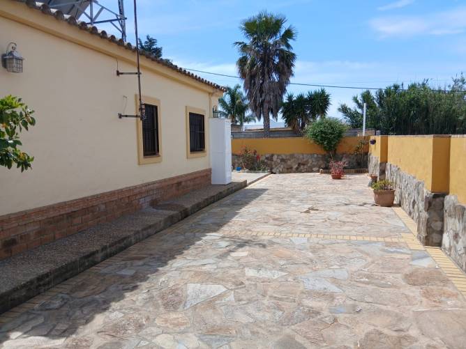 Patio trasero amplio con suelo de piedra y paredes amarillas junto a la vivienda