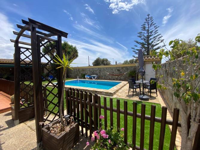Zona de piscina vallada con césped, muebles de exterior y plantas ornamentales