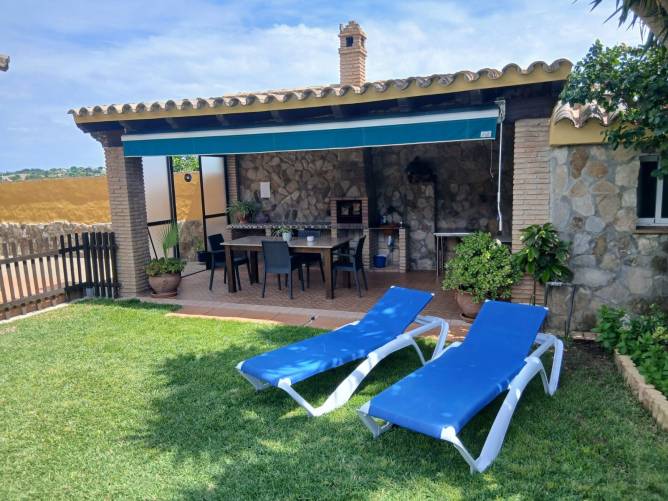 Jardín con tumbonas y vista al porche con barbacoa y mesa exterior