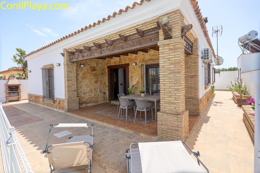 Porche amplio con mesa y sillas junto a barbacoa en patio lateral de la casa