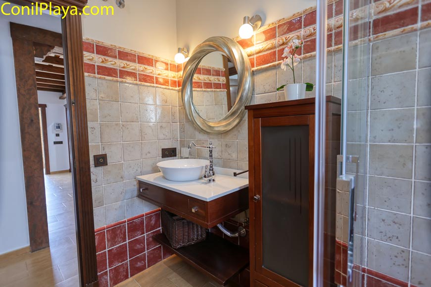 Lavabo de baño con espejo redondo y mueble de madera desde la entrada