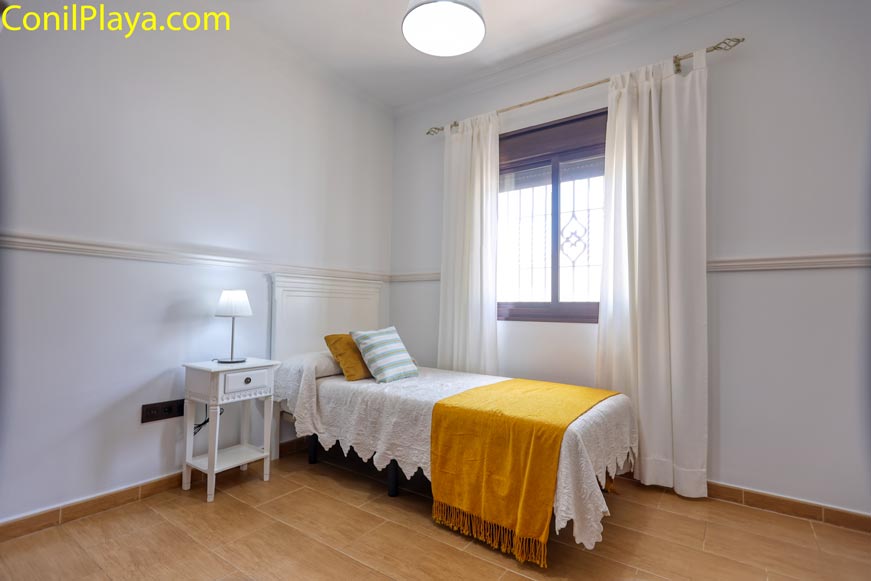 Dormitorio con una cama individual junto a la ventana y mesilla blanca