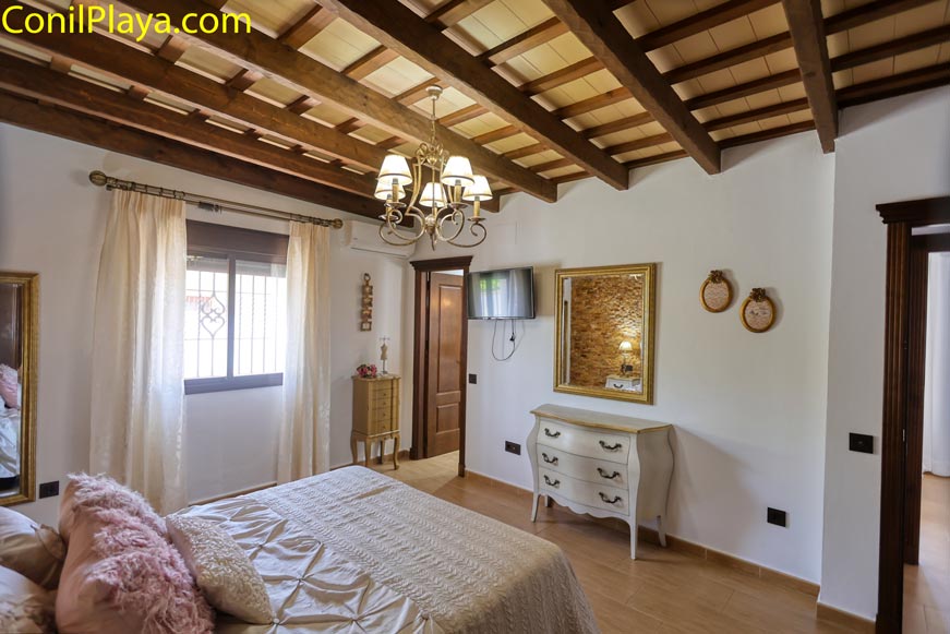 Dormitorio con cama, cómoda, ventana y vigas de madera visto desde la entrada