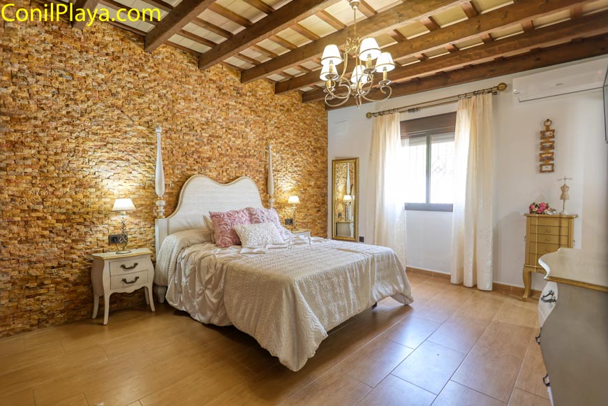 Dormitorio principal con pared de piedra, cama doble y muebles clásicos