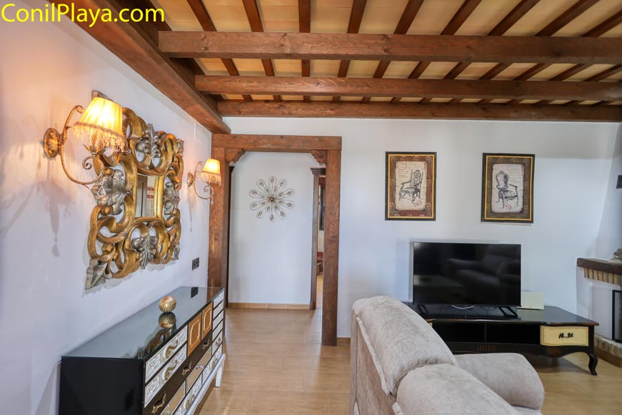 Salón con techo de vigas vistas, televisor y espejo decorativo dorado