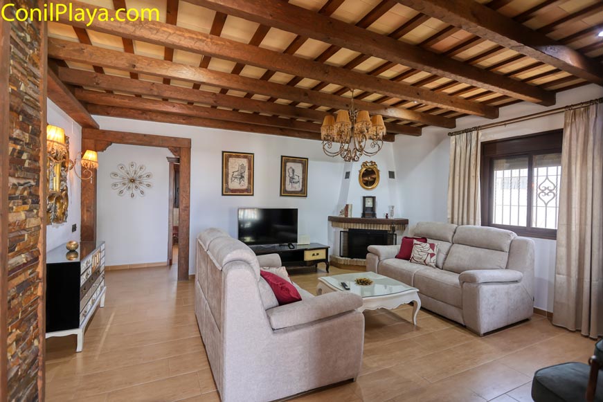 Salón amplio con sofás claros, chimenea y detalles rústicos en techo de madera