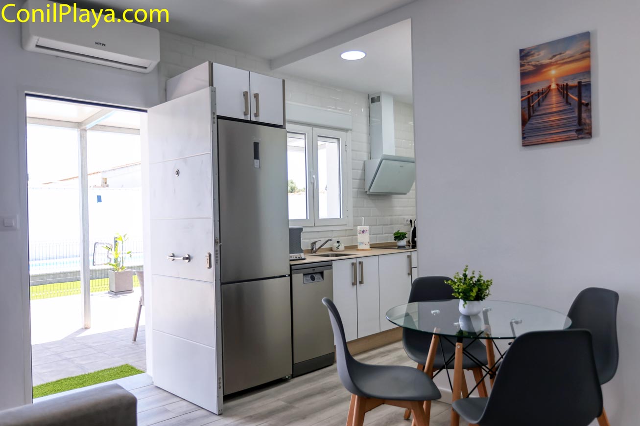 Comedor con mesa de cristal junto a cocina equipada y puerta abierta