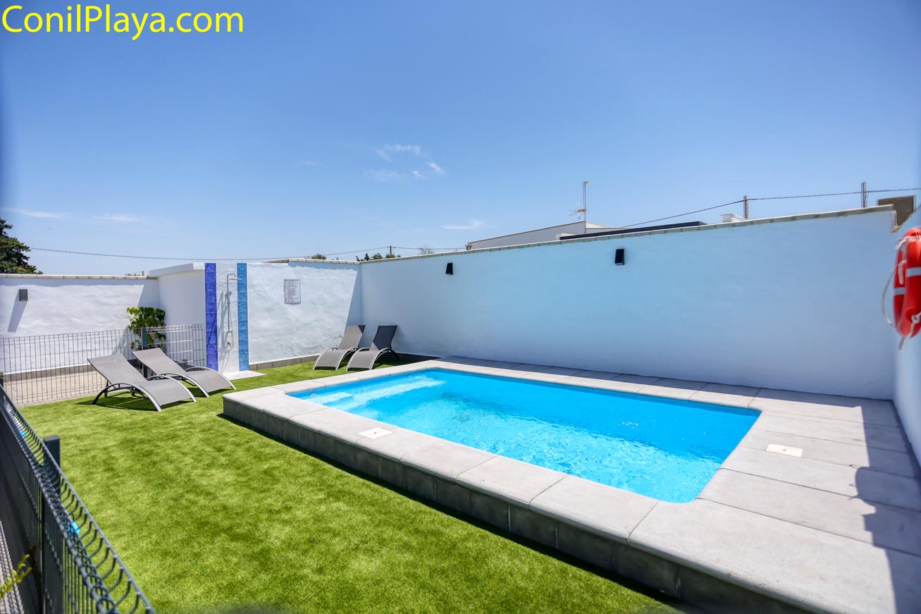 Piscina privada con zona de césped artificial y tumbonas vista desde la entrada
