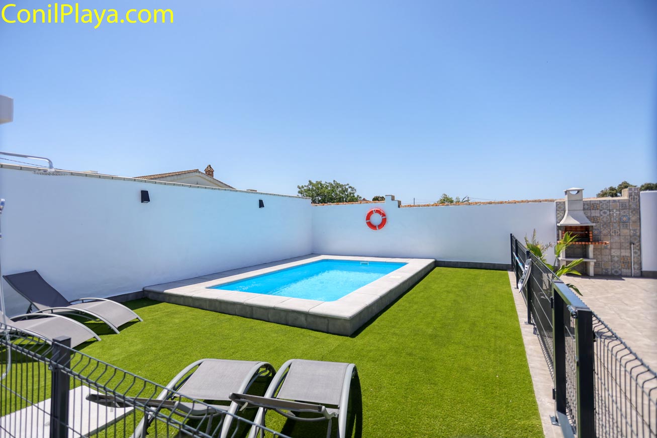 Zona exterior con piscina vallada, césped artificial y barbacoa de obra junto a pared