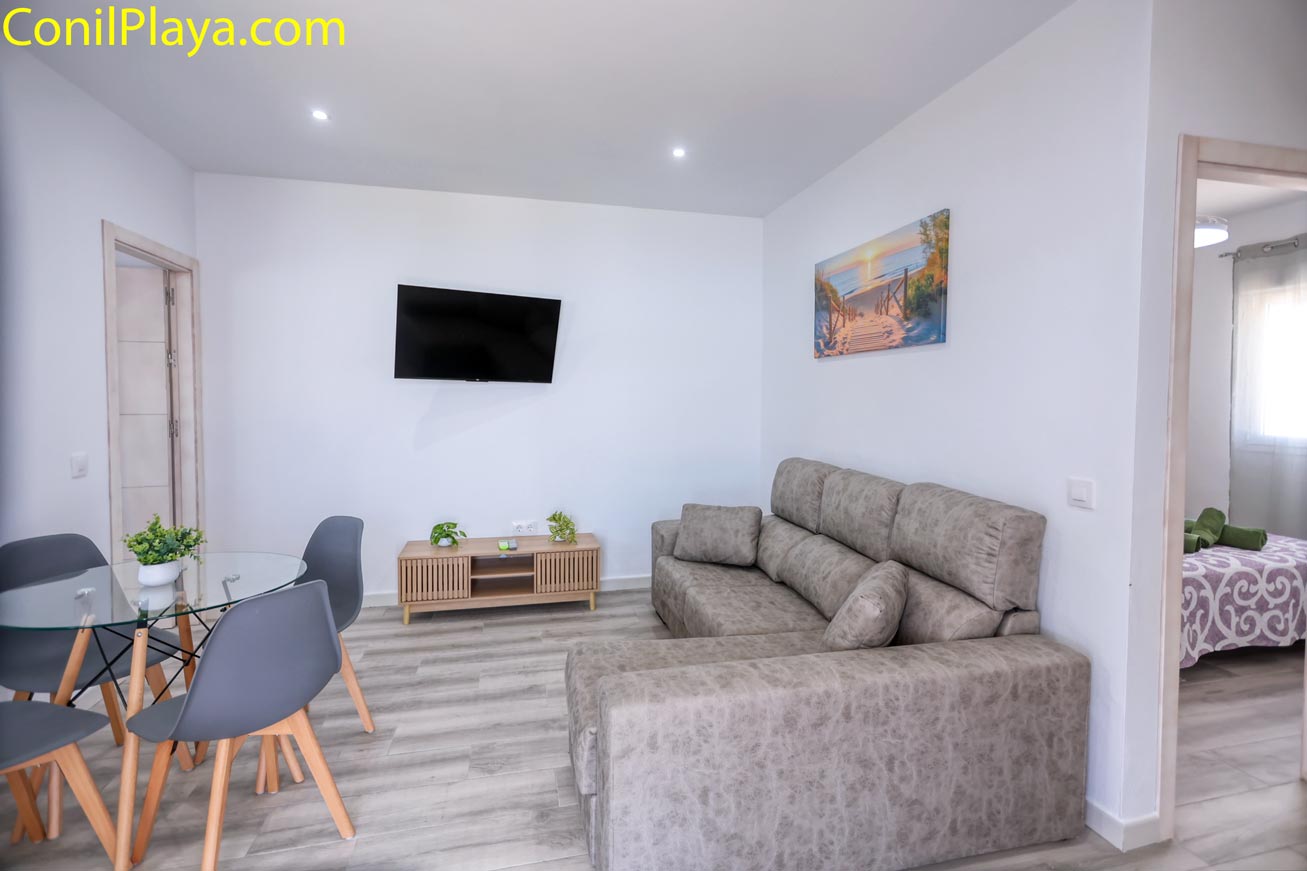 Salón moderno con sofá, mesa de cristal y televisor en la pared