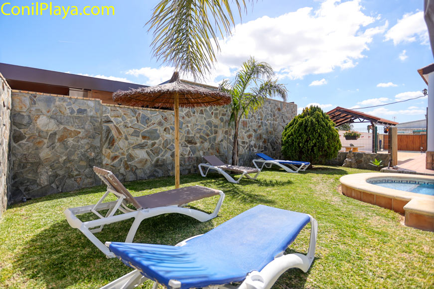 Jardín con tumbonas, sombrilla de paja y césped junto a piscina privada