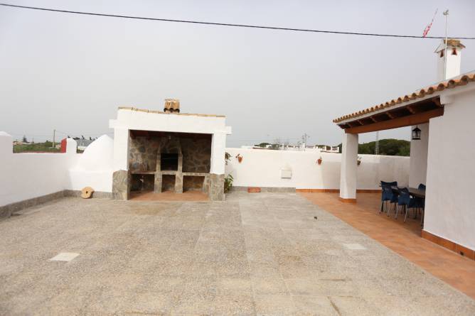 Barbacoa cubierta, con mesa y sillas y el chalet al fondo