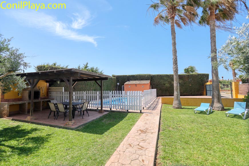 Zona de barbacoa cubierta junto a piscina vallada y césped cuidado