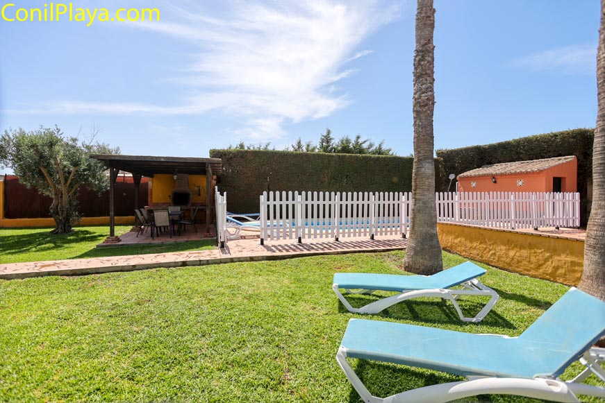 Jardín con tumbonas frente a piscina vallada y zona de comedor exterior